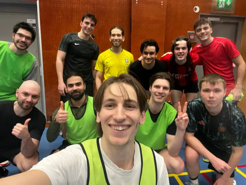 Smiling group selfie of a dozen players in bibs inside an indoor sports hall