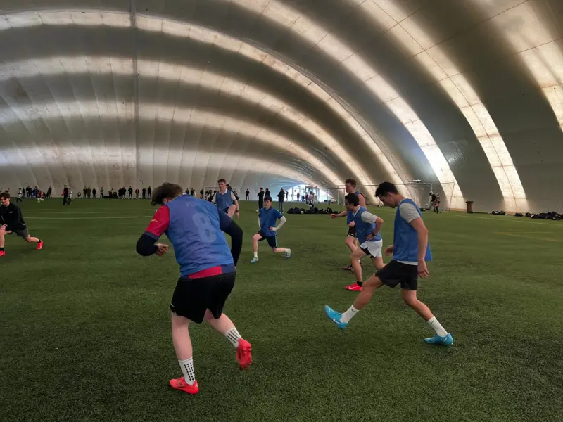 Players in blue bibs warming up on artificial turf under an inflatable dome