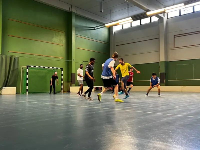 Player in a yellow shirt dribbling past defenders in a green indoor hall
